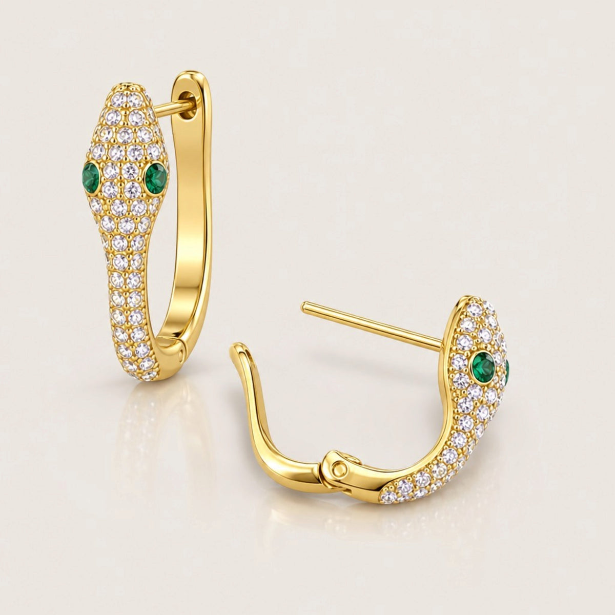 Gold pavé snake huggie pair with one upright and one open, showing green zircon eyes, straight posts, and bottom hinges.