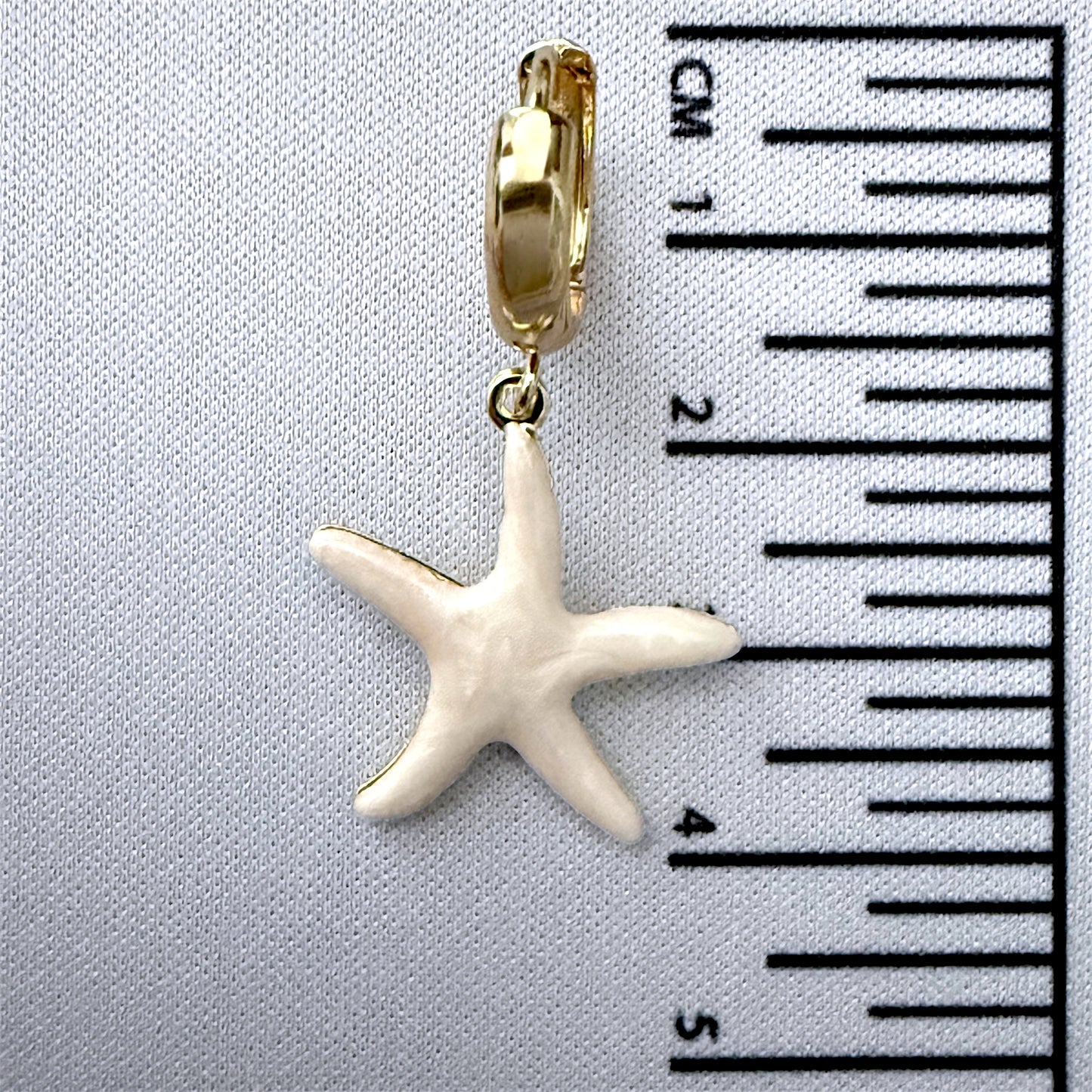 Starfish charm on a gold  with a ruler for scale on a gray background