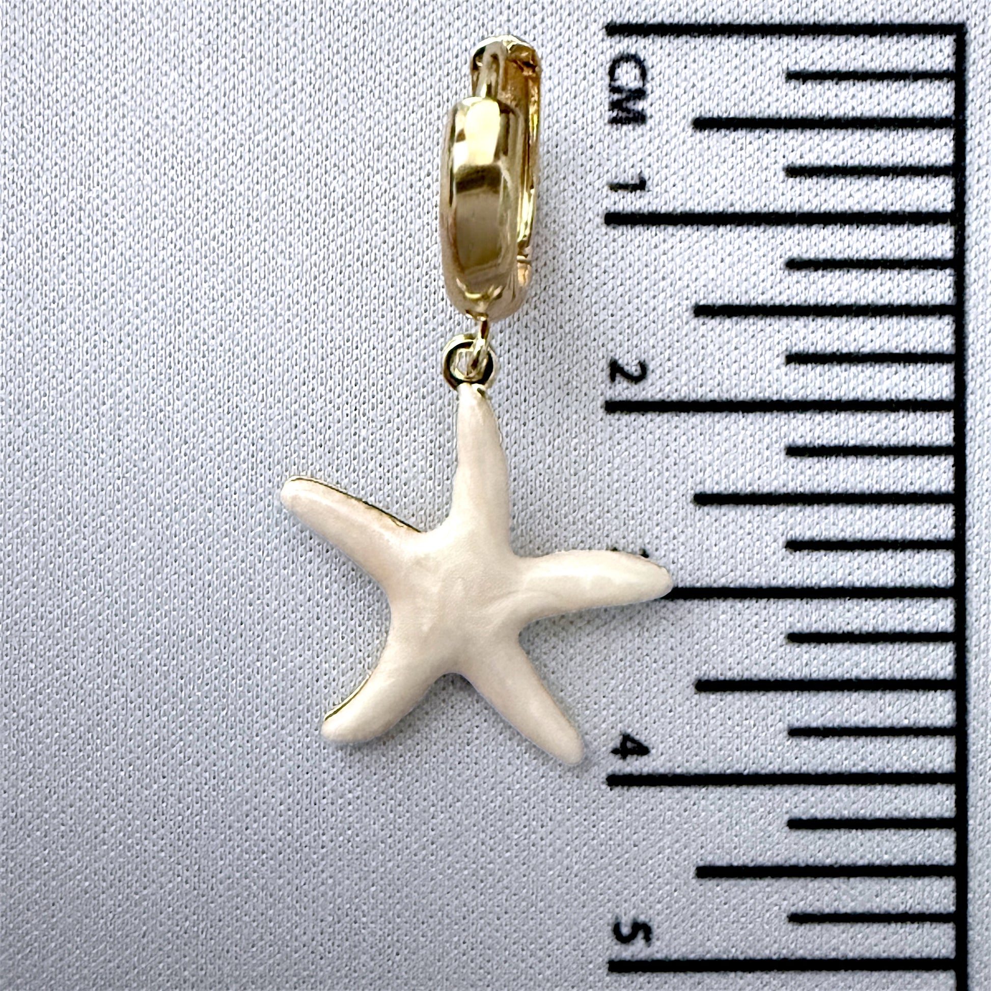 Starfish charm on a gold  with a ruler for scale on a gray background