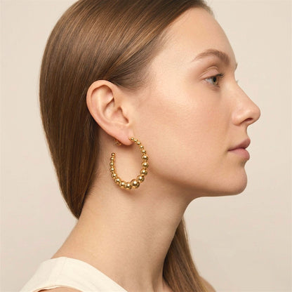 Model wearing a gold graduated beaded hoop earring, showing its open hoop shape and size beside the face.