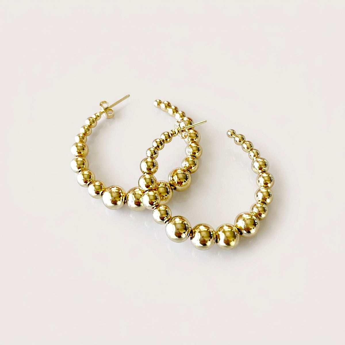 Pair of polished gold graduated beaded hoop earrings with overlapping hoops and visible post backs on a light background.