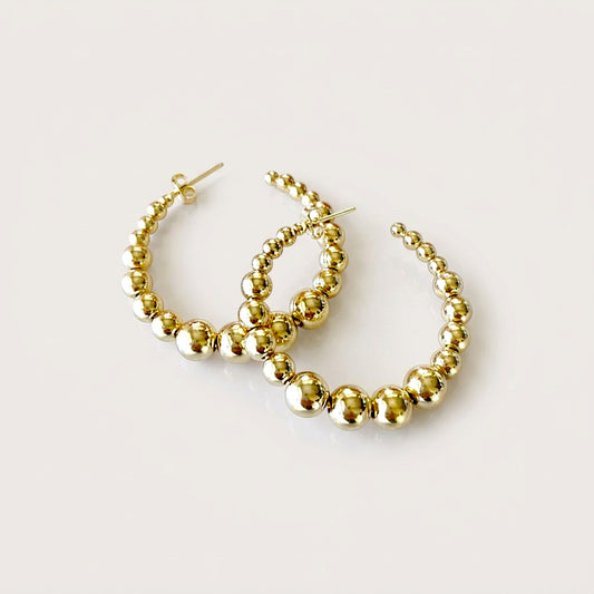 Pair of polished gold graduated beaded hoop earrings with overlapping hoops and visible post backs on a light background.