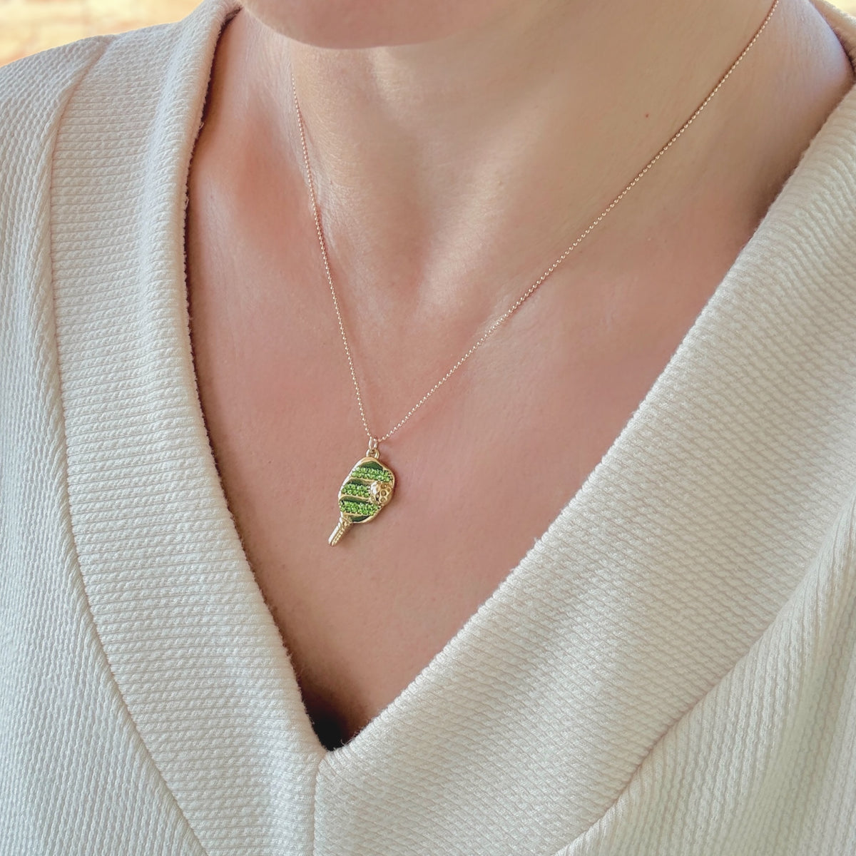 Model wearing the gold pickleball paddle charm necklace with green crystal accents, showing the delicate fit on the neckline.