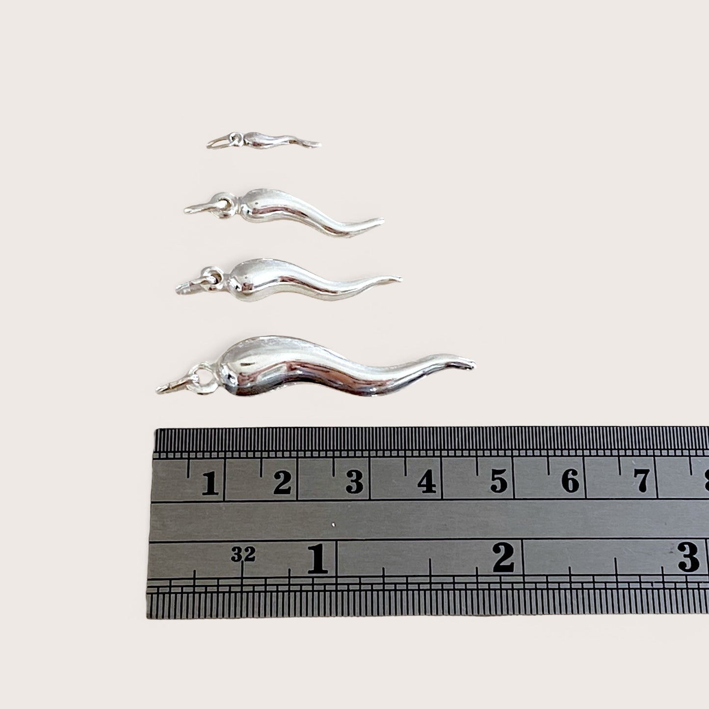 Real-world scale photograph showing the solid silver Italian horn pendant sizes lined up next to a steel ruler to verify precise metric measurements.