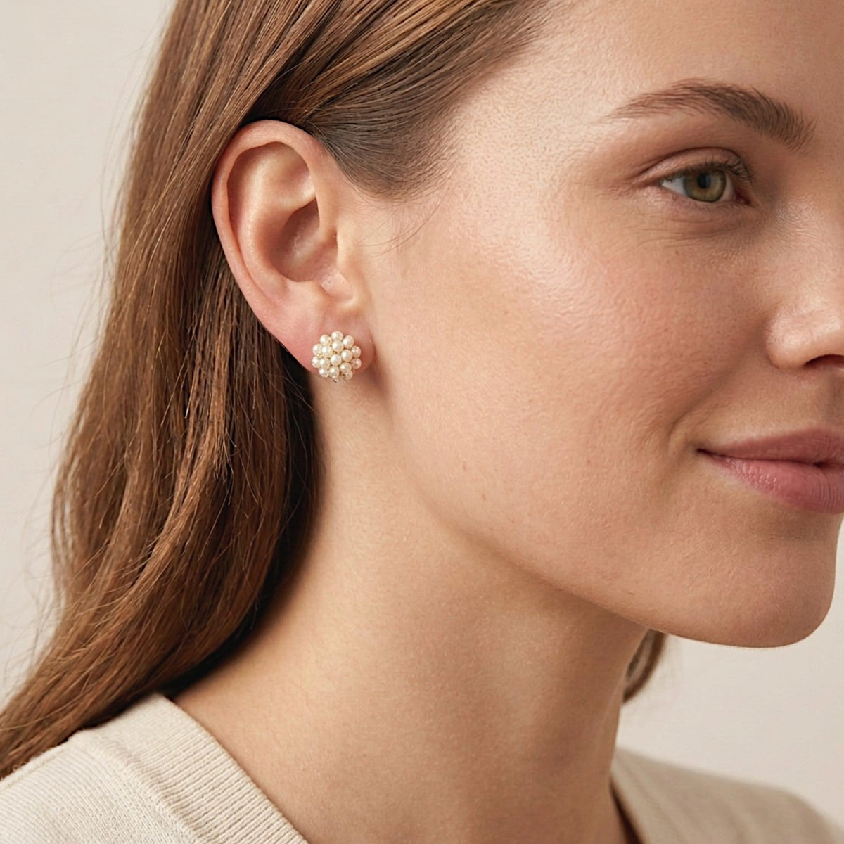 Woman with chestnut hair tucked behind her ear wearing an ivory pearl cluster stud earring and a cream knit top.
