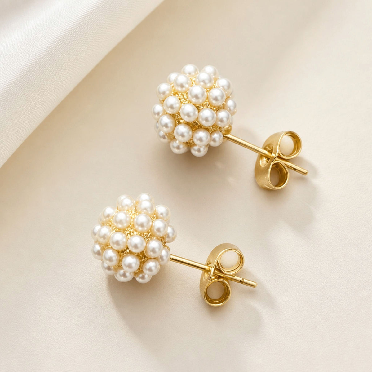Two rounded pearl cluster earrings arranged diagonally, showing the ivory pearls, gold settings, straight posts, and butterfly backs.