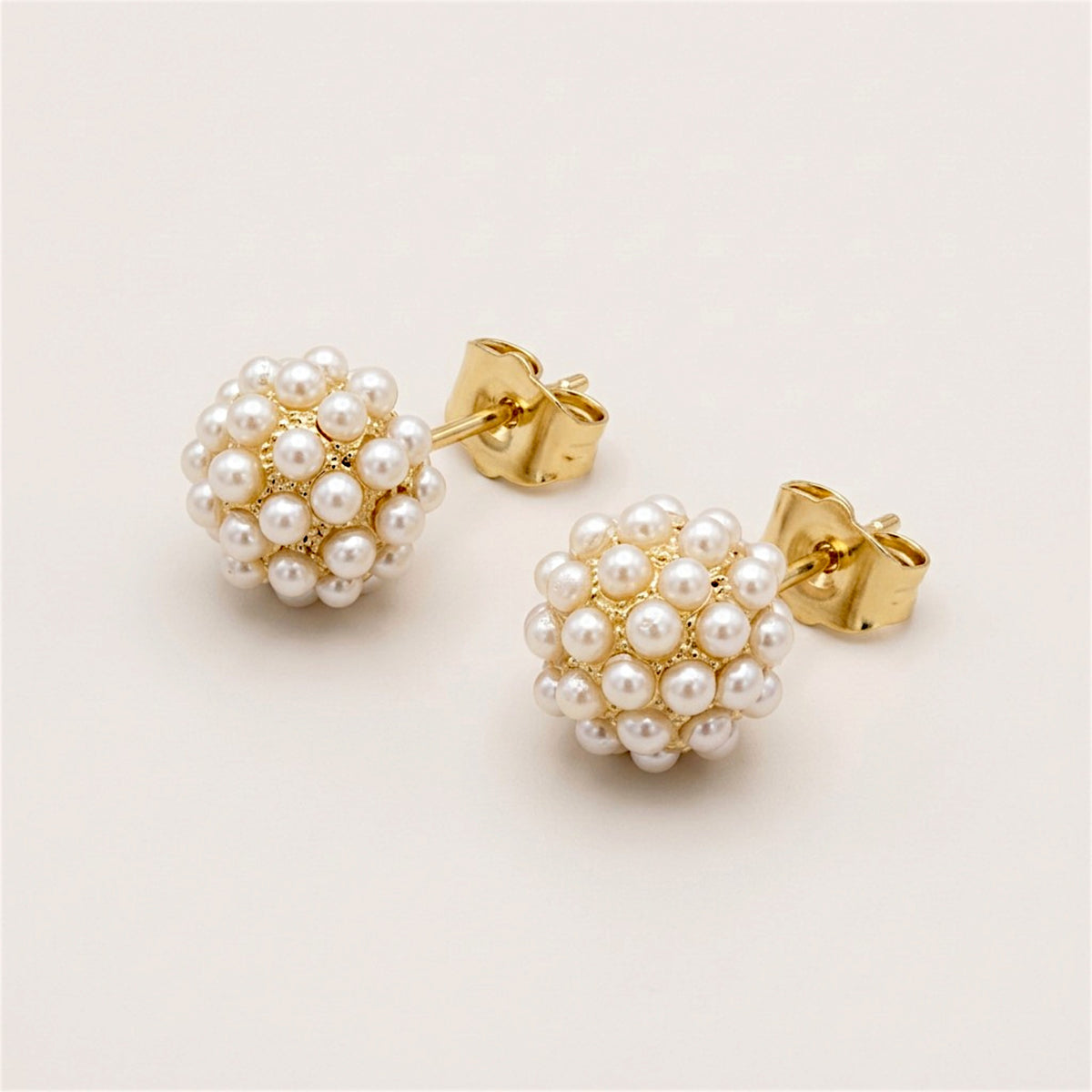 Pair of ivory pearl cluster stud earrings with fine gold detailing, shown at an angle with posts and butterfly backs visible.