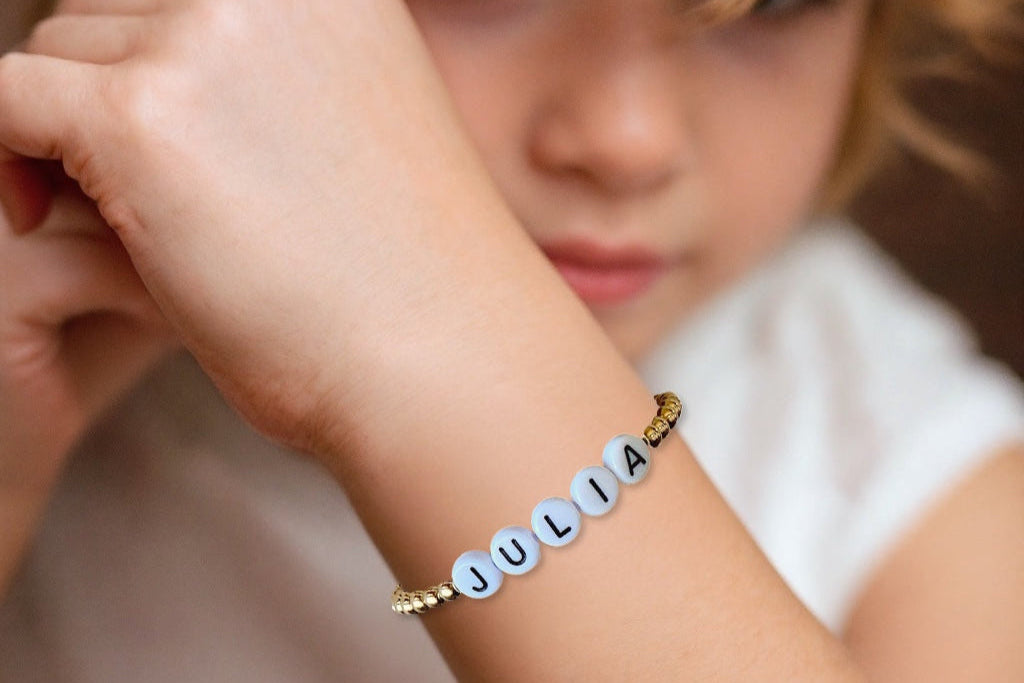 Child wearing a custom gold beaded bracelet with personalized name Julia pn wrist