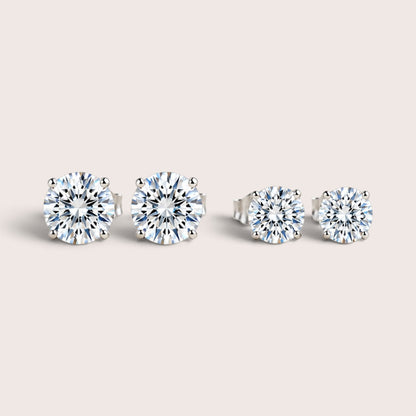 Two pairs of round moissanite stud earrings in silver settings, with the larger pair on the left and smaller pair on the right.