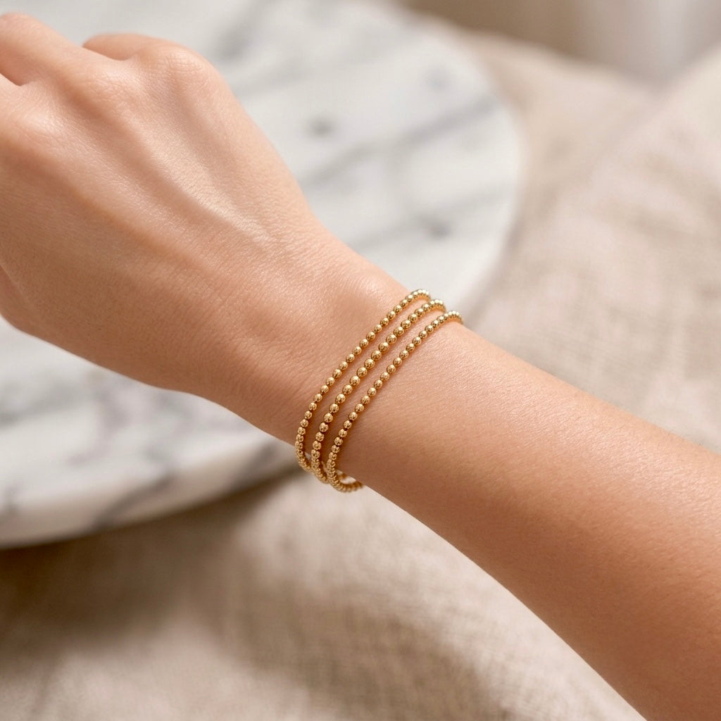 Lifestyle portrait of a model wearing multiple 14K gold-filled ball chain bracelets stacked together for a layered look.