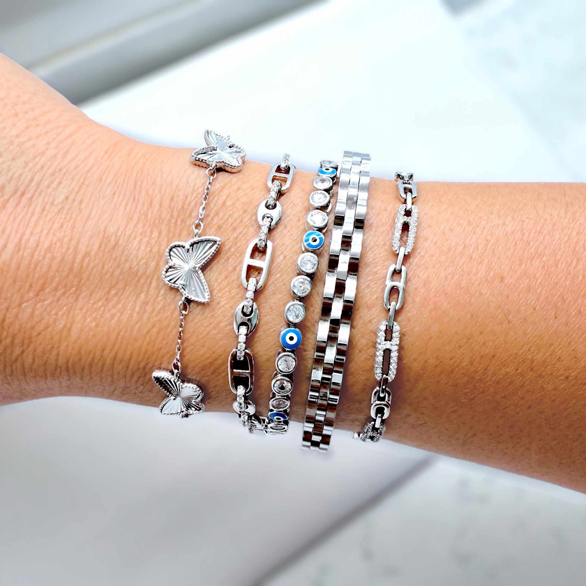 Wrist wearing multiple silver bracelets with butterfly and chain designs on a light background