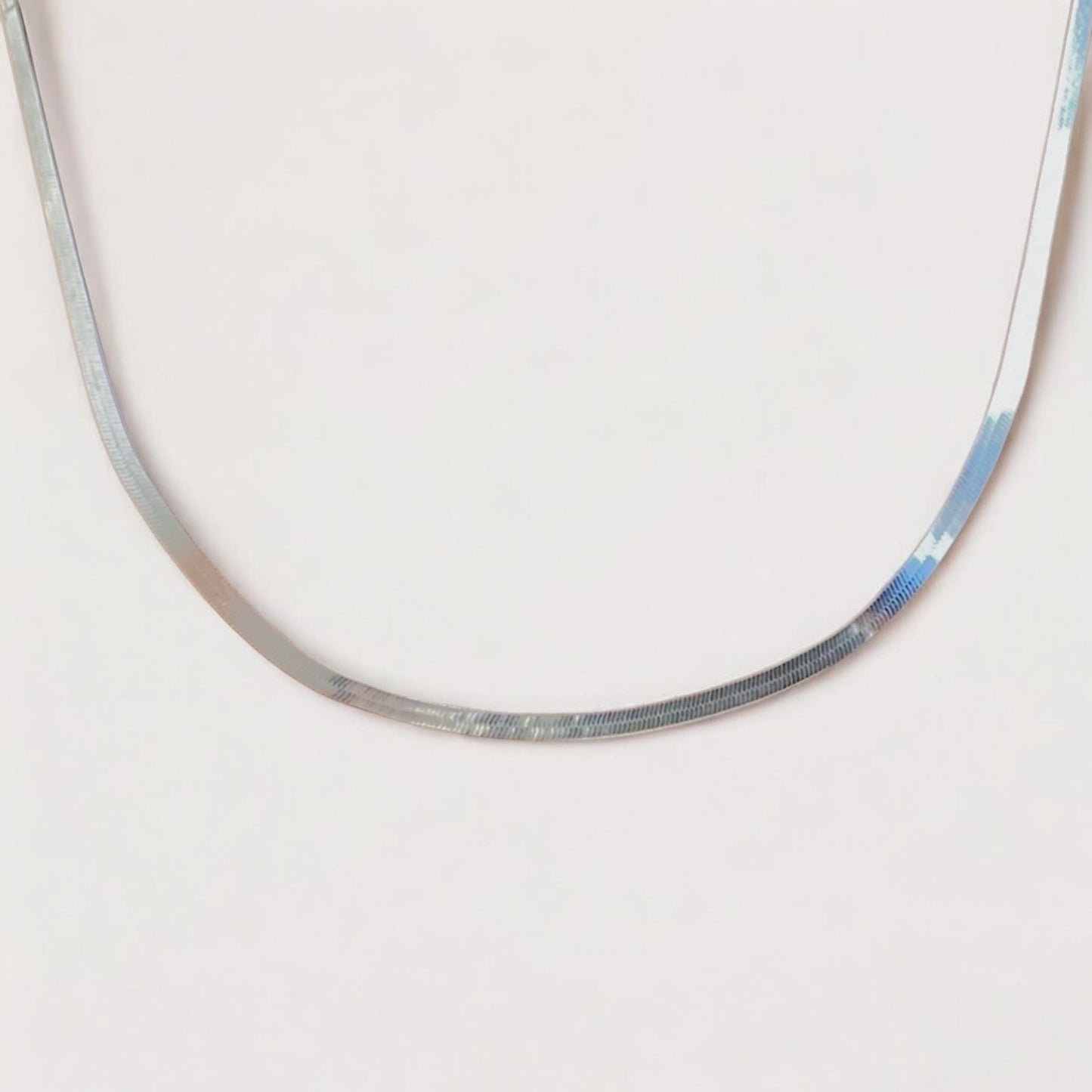 A close-up shot of  the 3.2mm unisex Italian sterling silver herringbone necklace, showcasing how the flat mirror chain elegantly lays flat and looks like a liquid silver