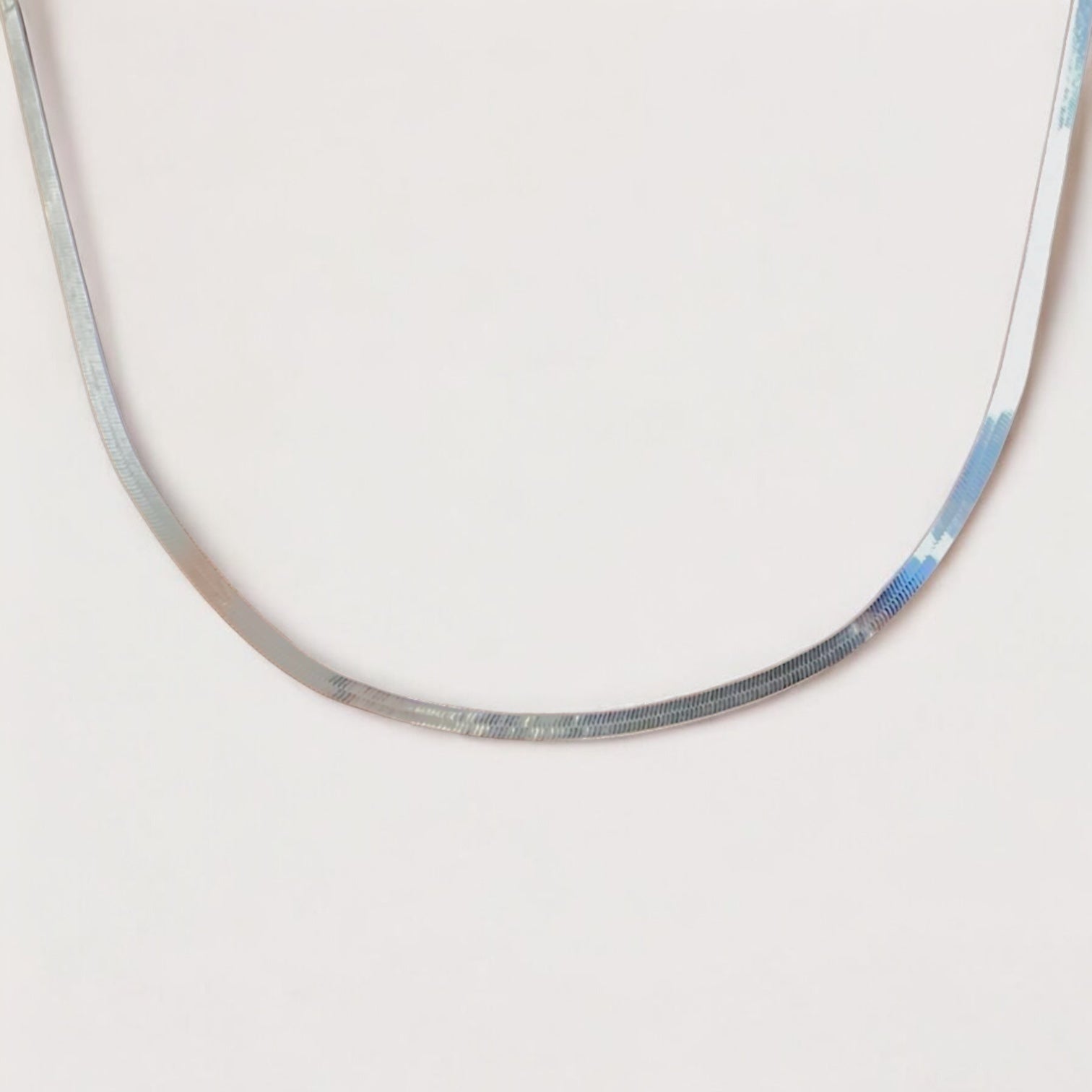 A close-up shot of  the 3.2mm unisex Italian sterling silver herringbone necklace, showcasing how the flat mirror chain elegantly lays flat and looks like a liquid silver
