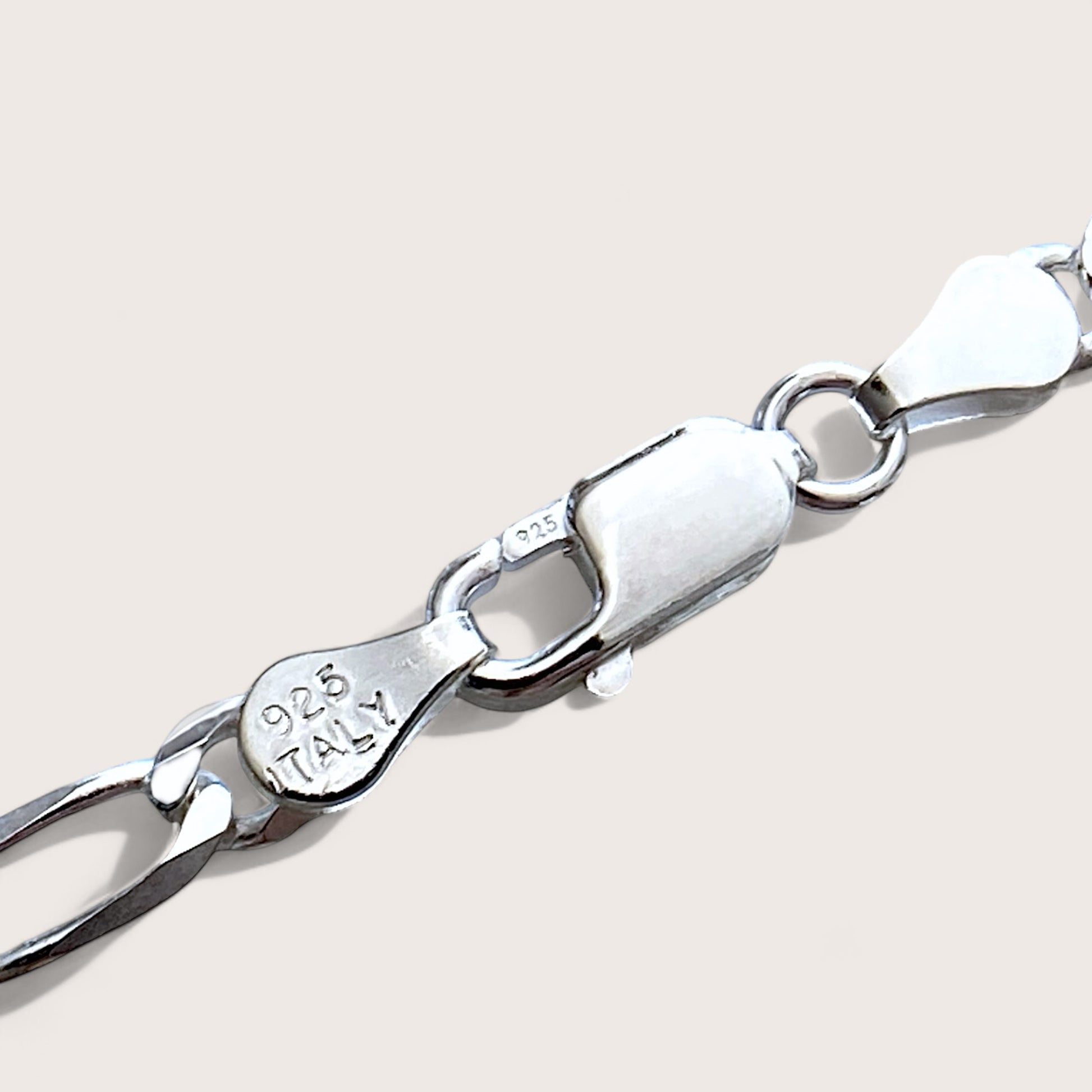 A close-up shot showcasing sterling silver Figaro chain bracelet showing the 925 Italy stamp and lobster clasp closure