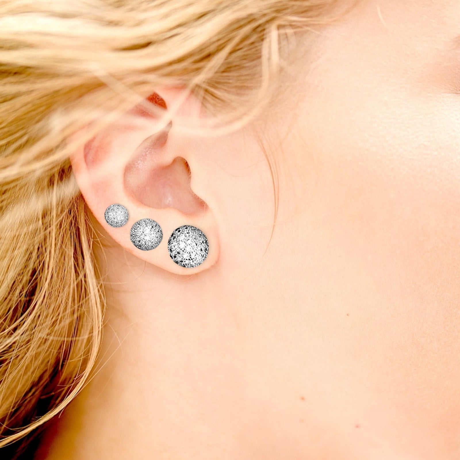 Close-up of a person wearing three silver earrings with different sizes shown on an ear.
