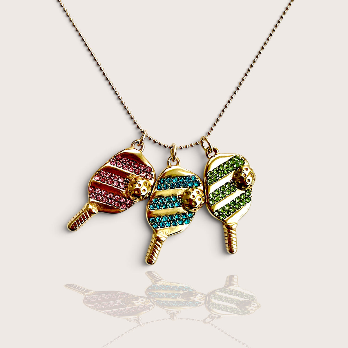 14K gold-filled pickleball paddle and ball charm necklace trio featuring Pink, Blue, and Green pavé cubic zirconia accents by Ashley Nicole Jewelry, front view.