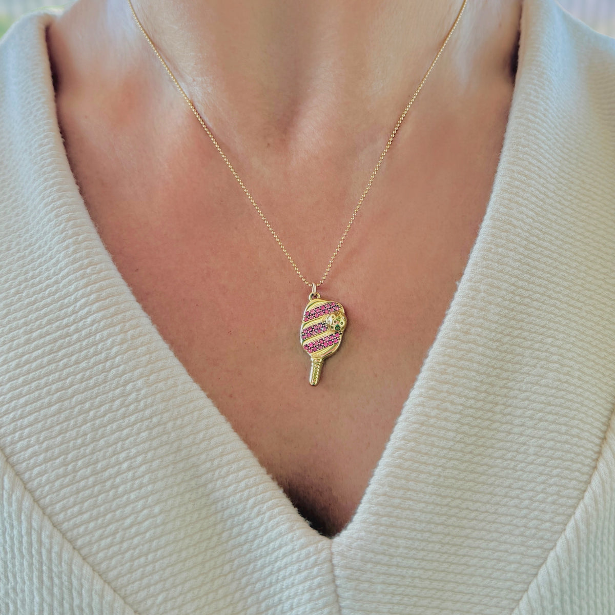 Model wearing the gold pickleball paddle necklace featuring pink pavé crystal accents.