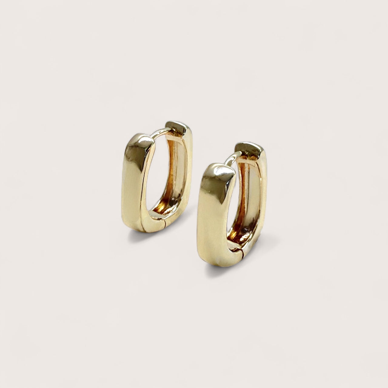 Pair of thick, chunky 18K gold plated 14mm rectangular huggie hoop earrings by Ashley Nicole Jewelry shown in a three-quarter studio view against a clean light beige background.