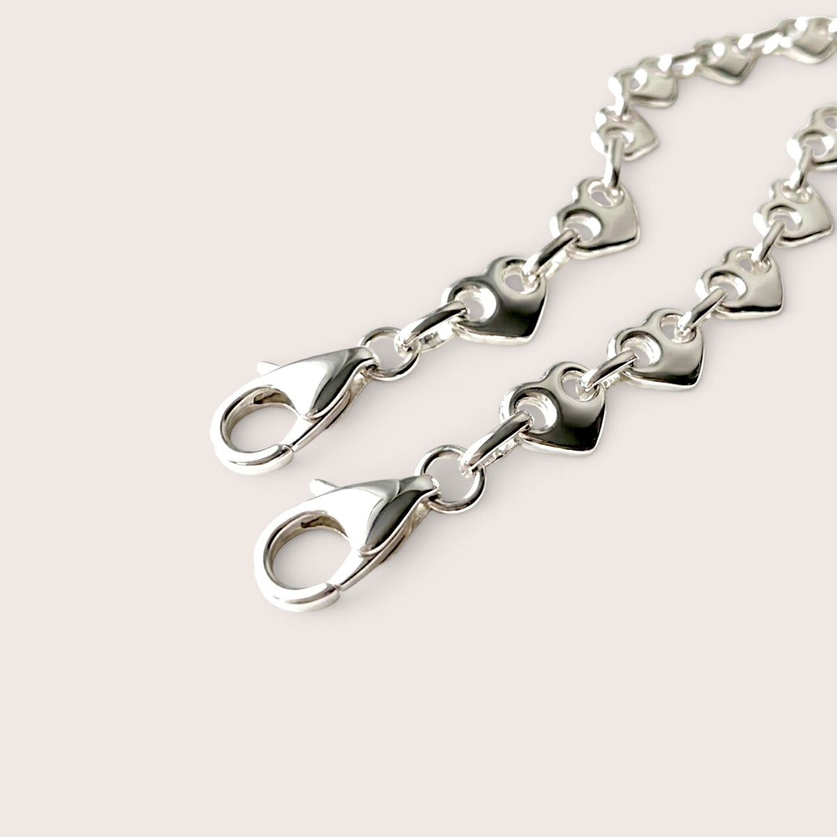 Close-up of two silver heart link bracelets showing their lobster clasps and connecting rings.