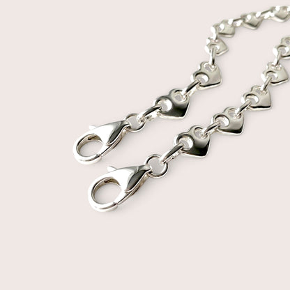Close-up of two silver heart link bracelets showing their lobster clasps and connecting rings.