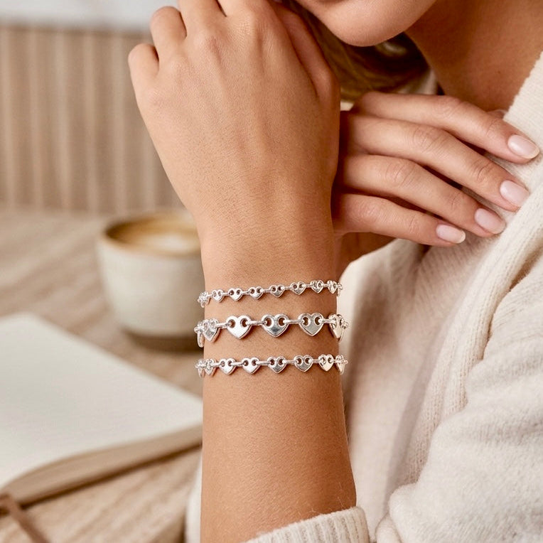 Model wearing three silver heart link bracelets in different widths with a cream blouse.