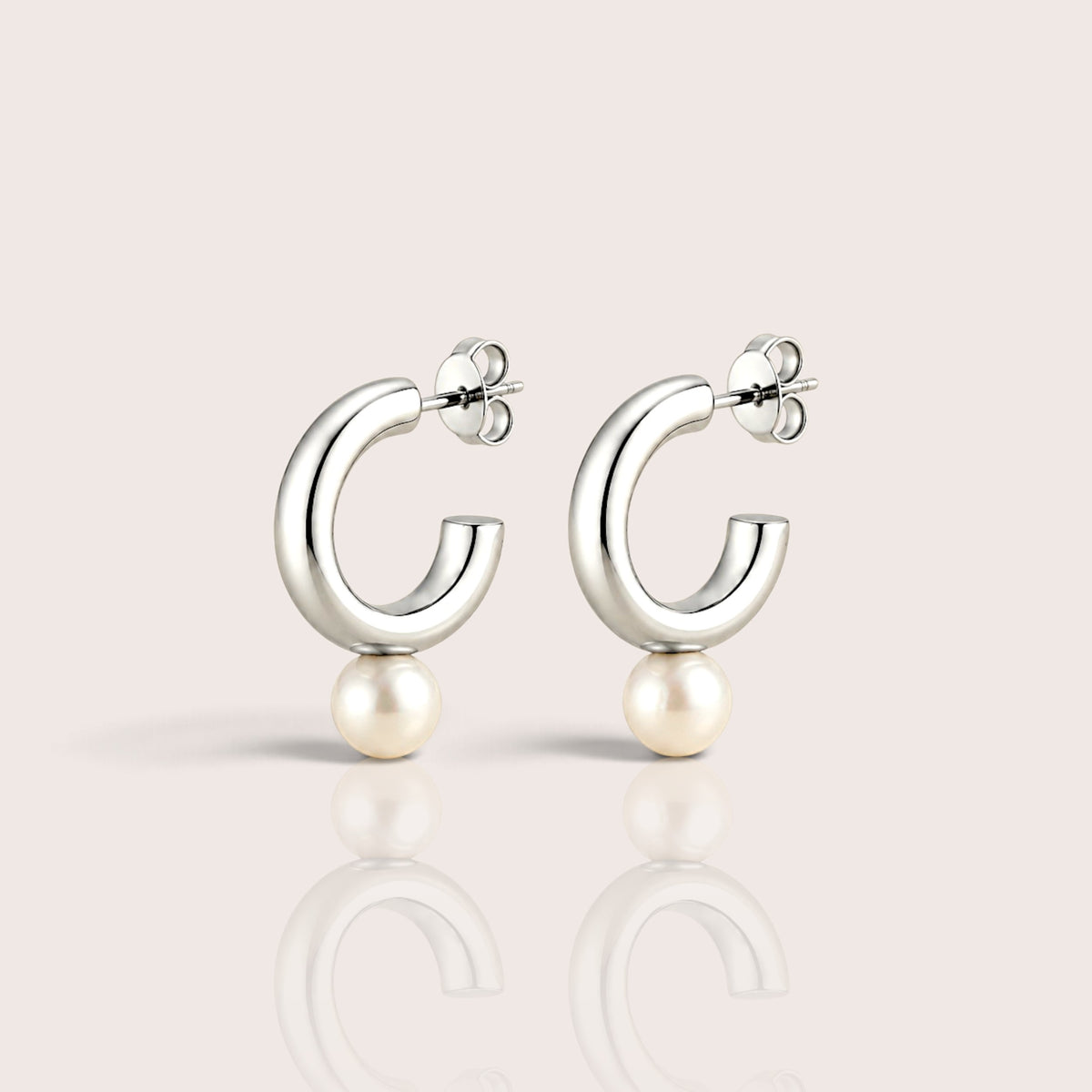 Pair of chunky silver open C hoop earrings with white pearl drops, shown on an ivory surface with soft shadows and reflections.
