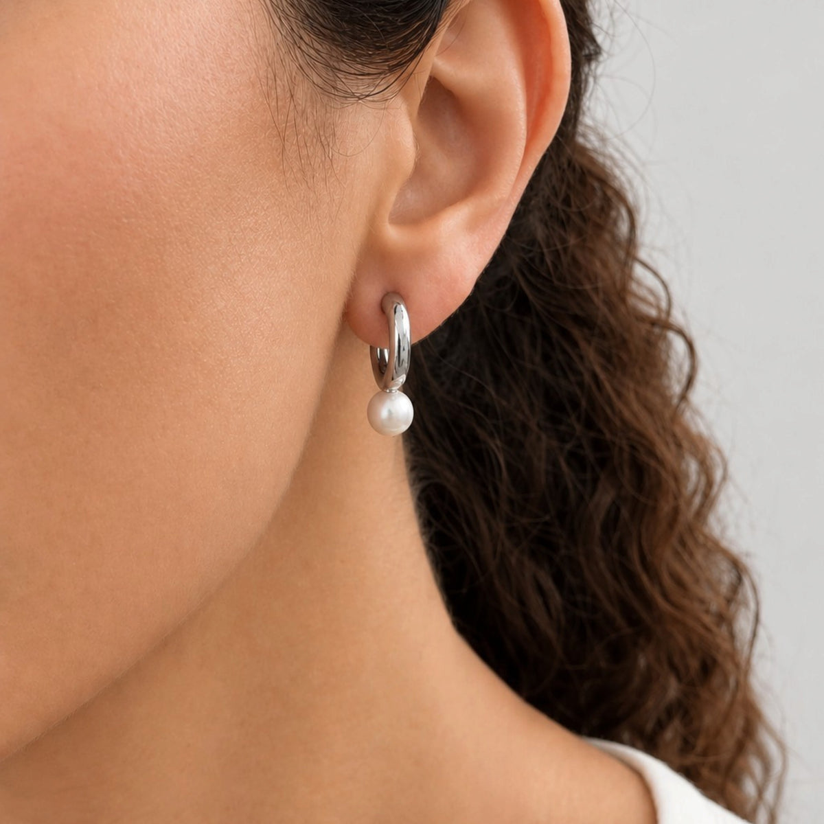Close-up side view of a model wearing a silver tube hoop earring with a white pearl drop.