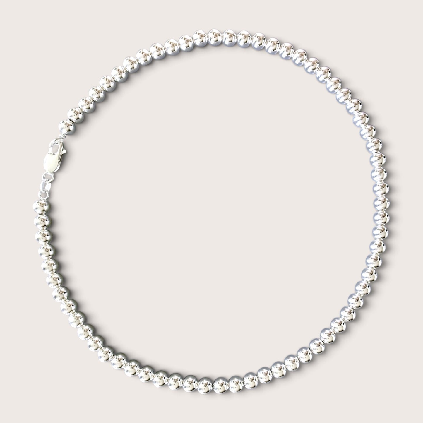 Flat lay of a solid 925 sterling silver 6mm round bead necklace over a black v-neck top against a warm minimalist studio background. The beads have a mirror-bright shine and are precisely scaled to 6mm.