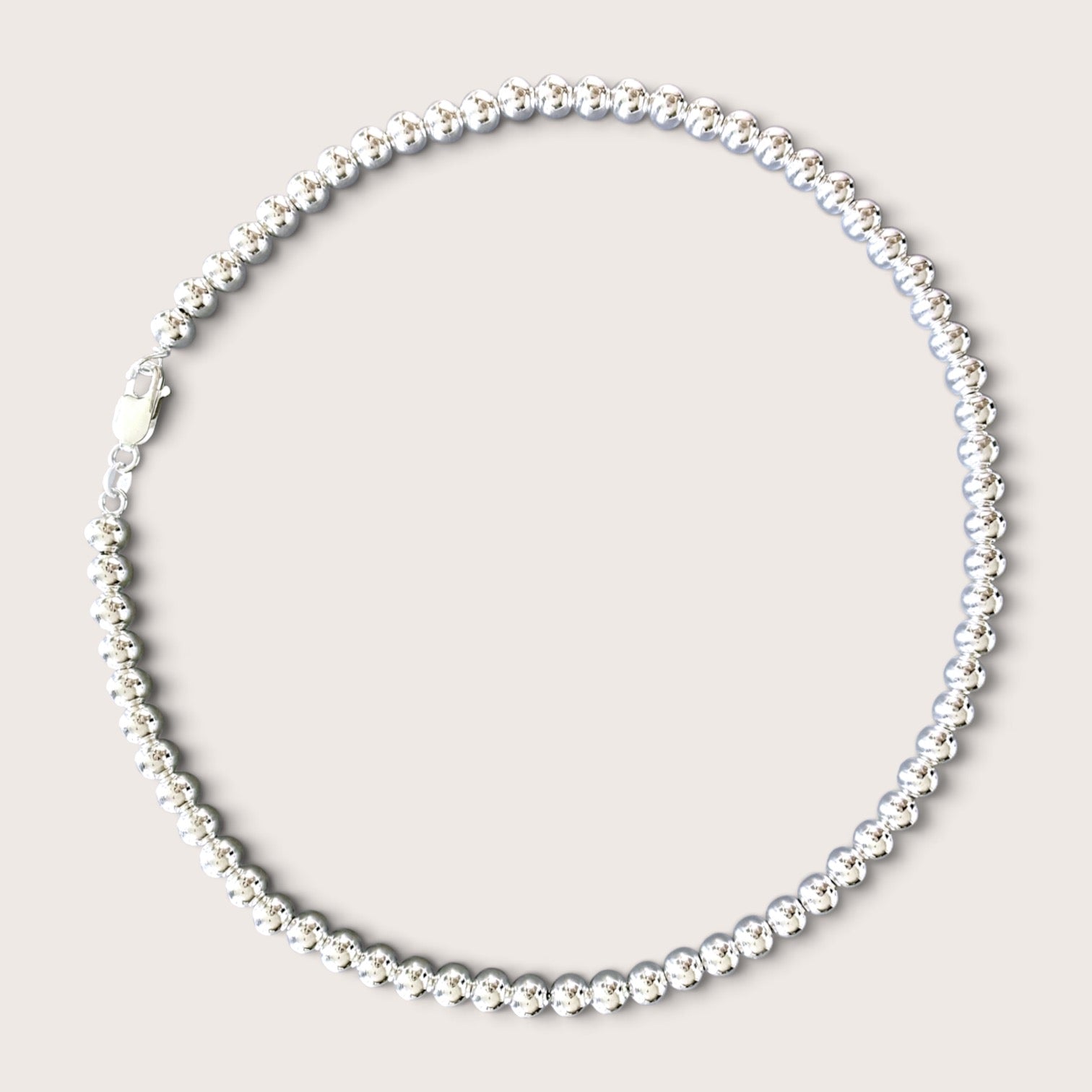 Flat lay of a solid 925 sterling silver 6mm round bead necklace over a black v-neck top against a warm minimalist studio background. The beads have a mirror-bright shine and are precisely scaled to 6mm.