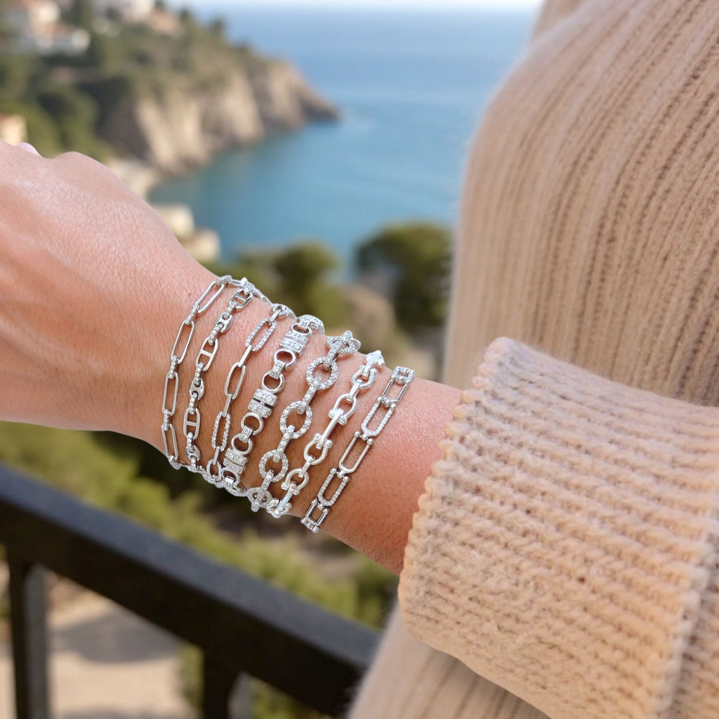 Stacked Silver chain bracelets on a wrist with a scenic background
