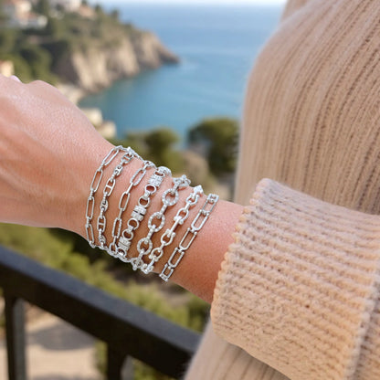 Stacked Silver chain bracelets on a wrist with a scenic background