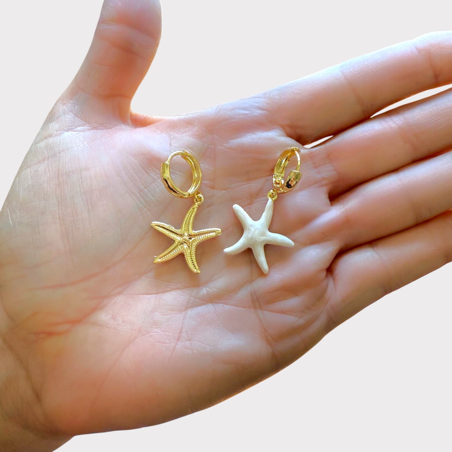 Gold and white starfish-shaped earrings held in a hand showing front and back side of the dangle charm 