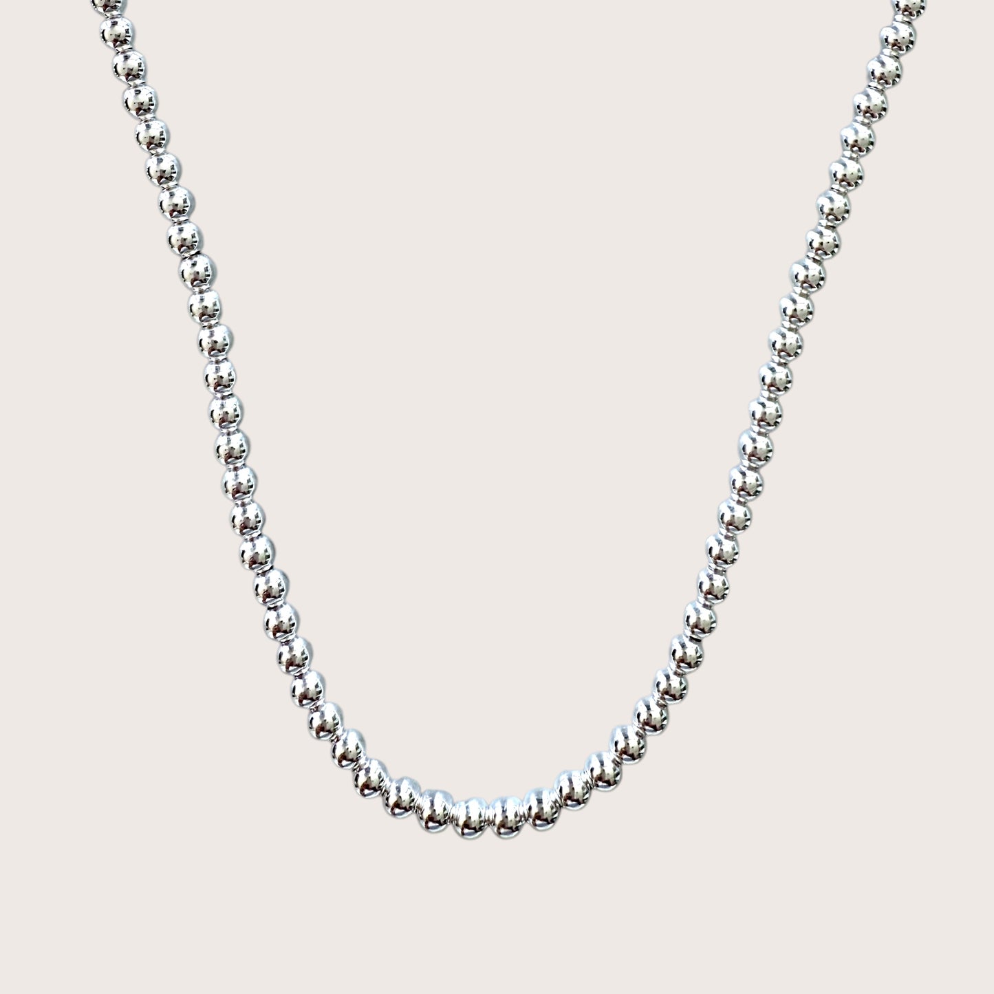 A sterling silver ball chain necklace with 5mm beads laid out on a plain background.