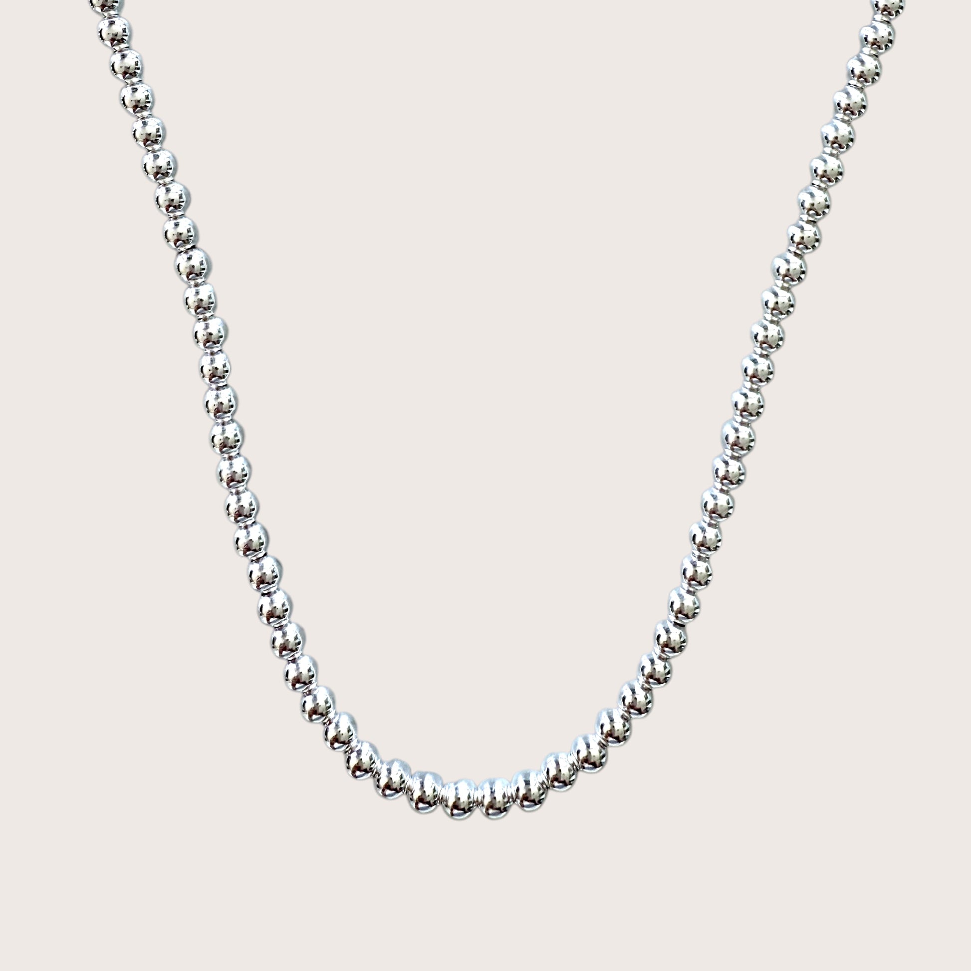 A sterling silver ball chain necklace with 5mm beads laid out on a plain background.