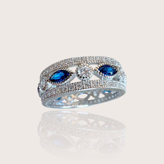 A sterling silver eternity ring with a central blue sapphire surrounded by smaller clear cubic zirconia stones, set in a marquise and round cut design.