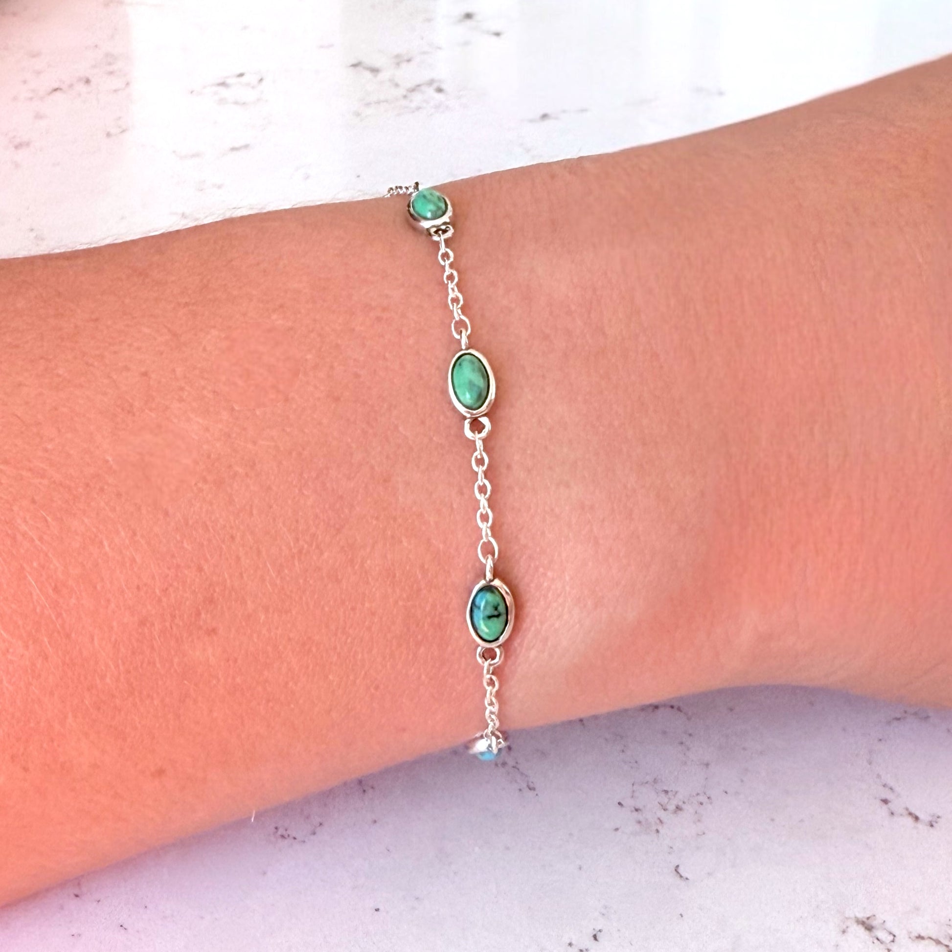 Silver bracelet with green beads on a wrist against a light background