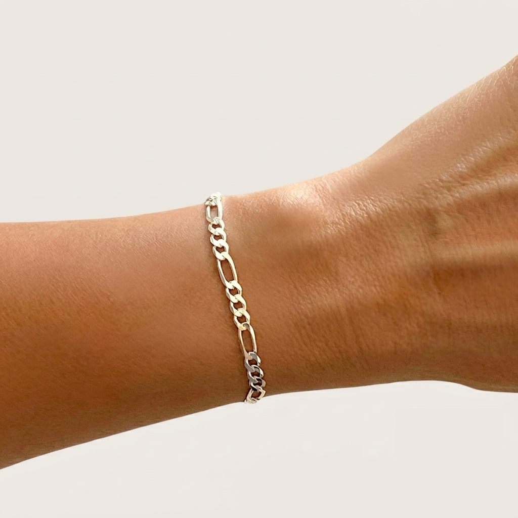 A close-up lifestyle shot showcasing the 4mm unisex sterling silver Figaro chain bracelet worn elegantly on a wrist, demonstrating how the links lay perfectly flat against the skin.