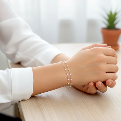 Close-up of a person's hand wearing a pearl bracelet on a blurred indoor background