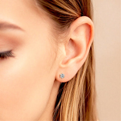 Small white gold diamond flower stud earring worn on an ear