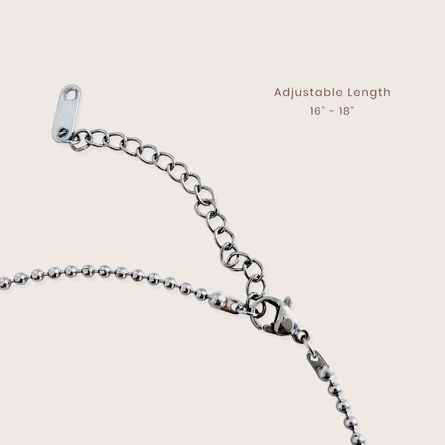 Close-up of a silver metal chain necklace extender with a lobster clasp and adjustable tag, shown on a light beige background with text reading 'Adjustable Length 16" - 18"'.