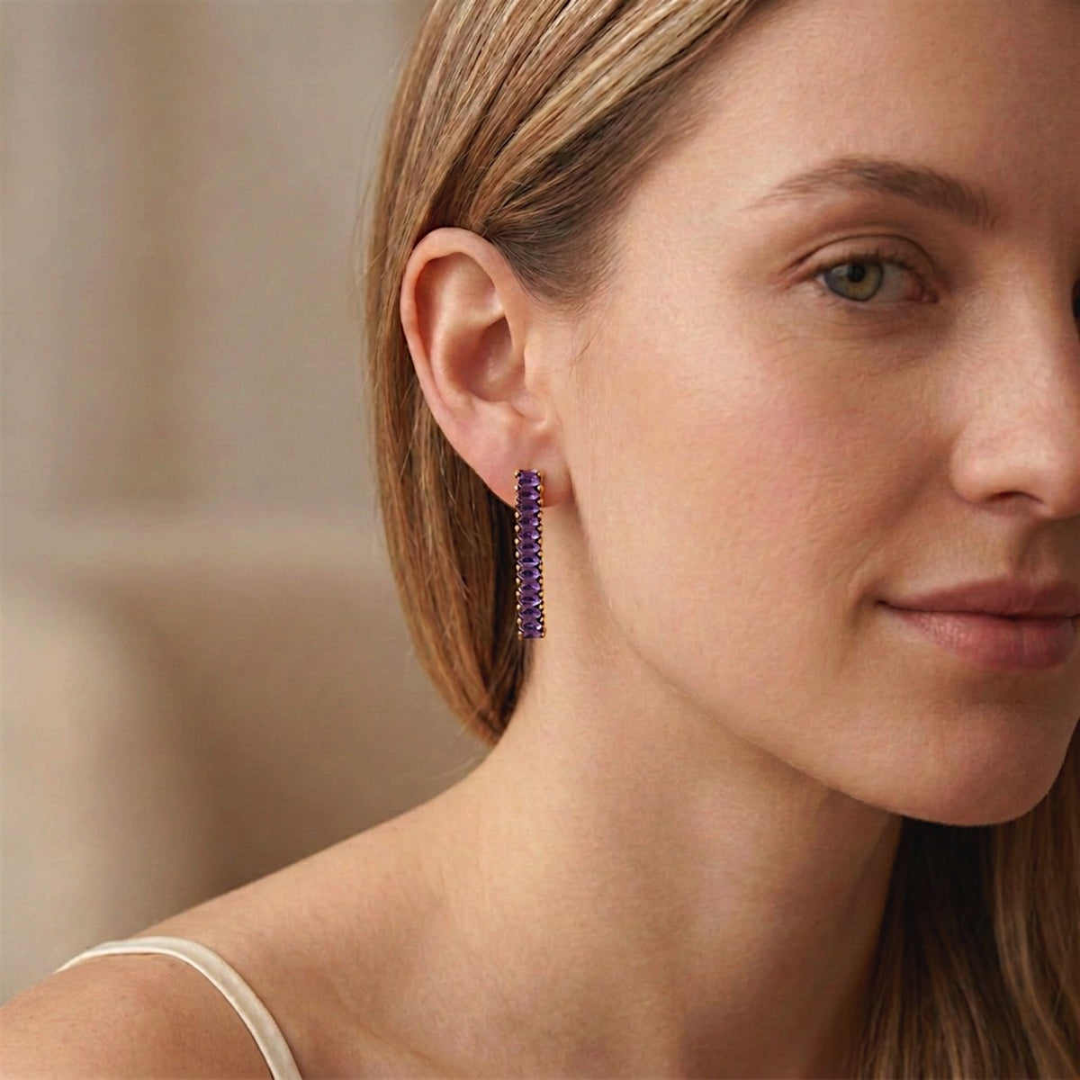 Close-up of a woman wearing an amethyst-purple baguette CZ drop earring with gold-tone settings.
