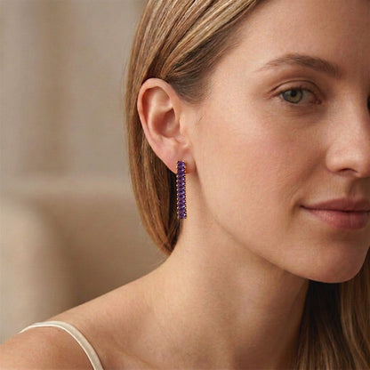 Close-up of a woman wearing an amethyst-purple baguette CZ drop earring with gold-tone settings.