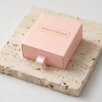 Pink Ashley Nicole Jewelry drawer-style gift box with a ribbon pull on a stone surface