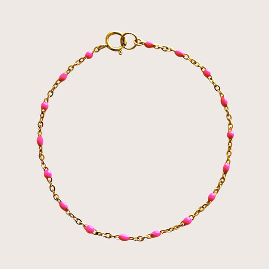 Flat lay view of a bright pink enamel beaded satellite bracelet in 14K gold filled hardware.