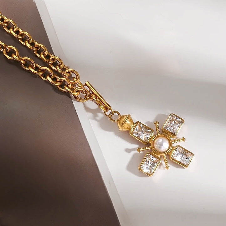 A thick gold cross necklace featuring four emerald cut rectangle crystals and central white fresh water pearl, with a front facing t-bar toggle clasp