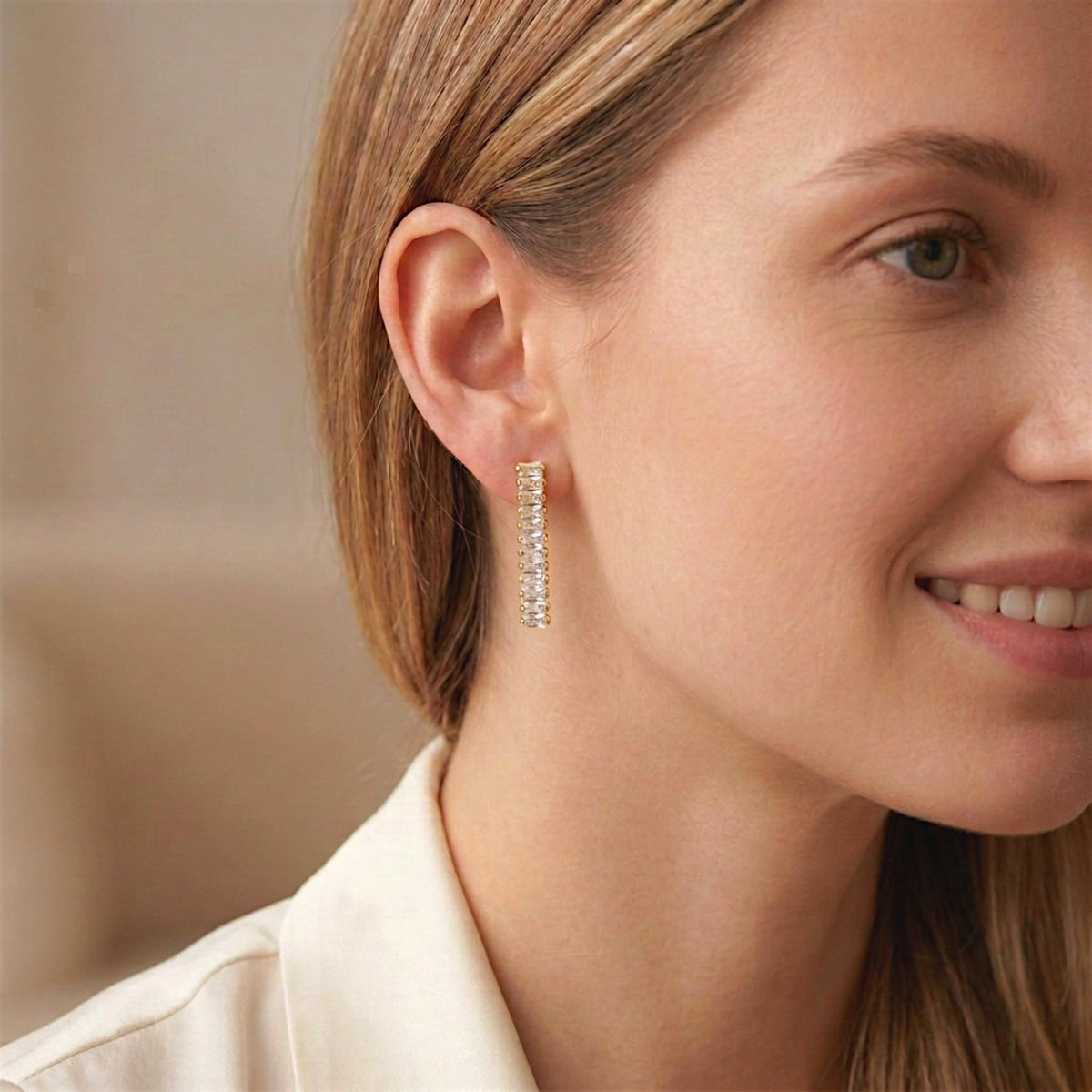 Close-up of a woman wearing a clear baguette CZ drop earring with gold-tone settings.