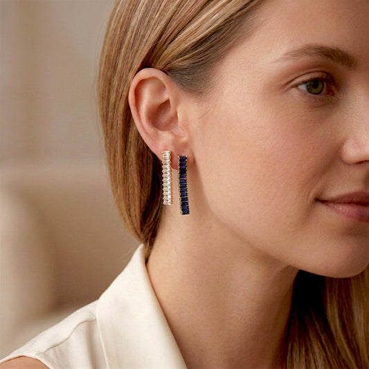 Clear and sapphire-blue baguette drop earrings with gold-tone settings worn together in two adjacent lobe piercings.