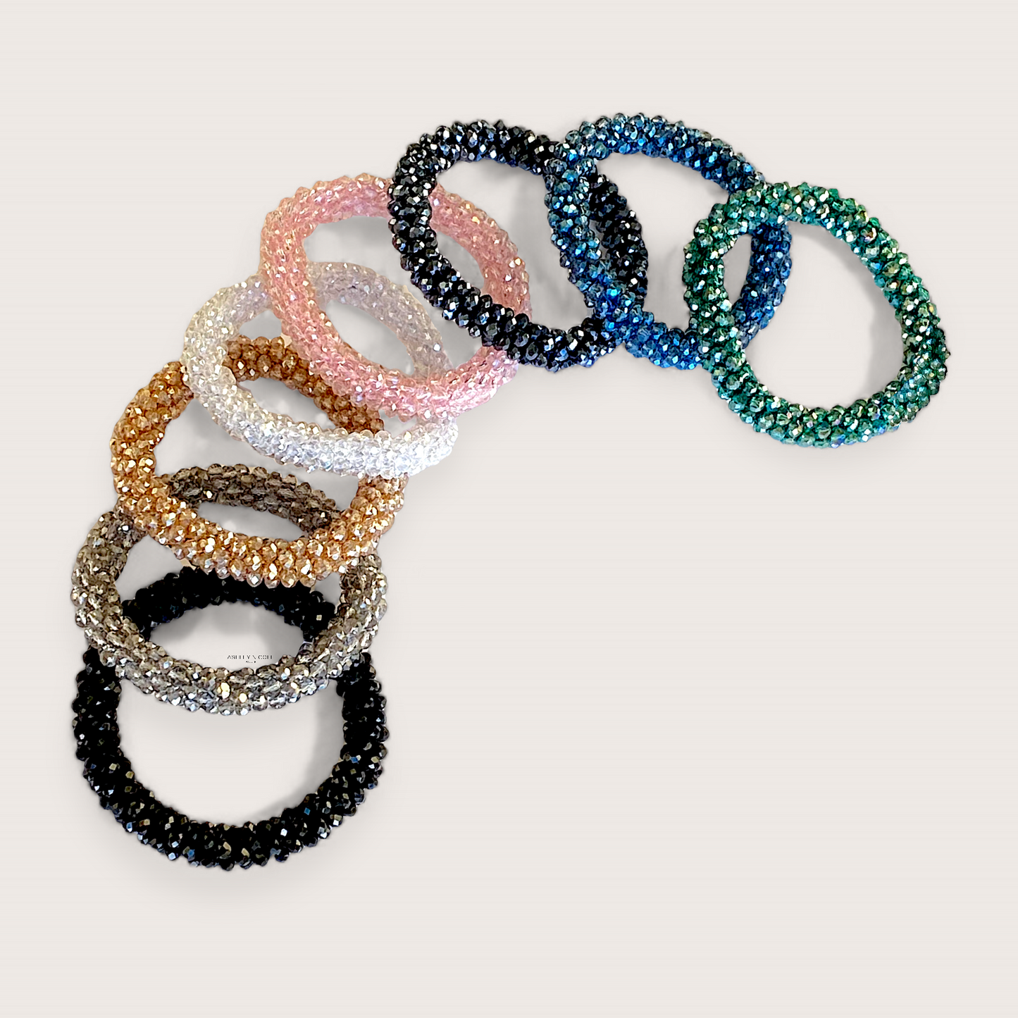 A collection of crystal bead elastic hair ties laid flat on a clean background showing the multi-faceted in black, silver, gold, teal blue, white, and pink, glass beads and woven stretch band by Ashley Nicole Jewelry. 