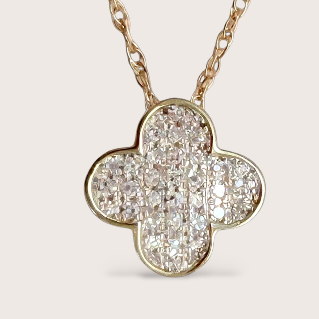 Close up of dainty 14k solid gold necklace with a diamond-encrusted clover pendant on a delicate gold chain. 