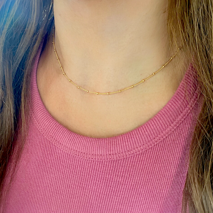 A close up of a person wearing a delicate gold chain necklace in a choker length